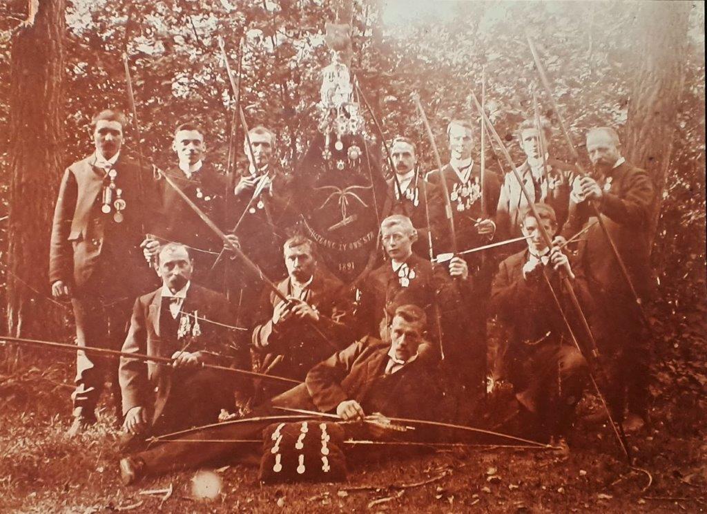Historische foto uit 1901 van leden van de VZOS met hun bogen en in het midden het vaandel van de vereniging.